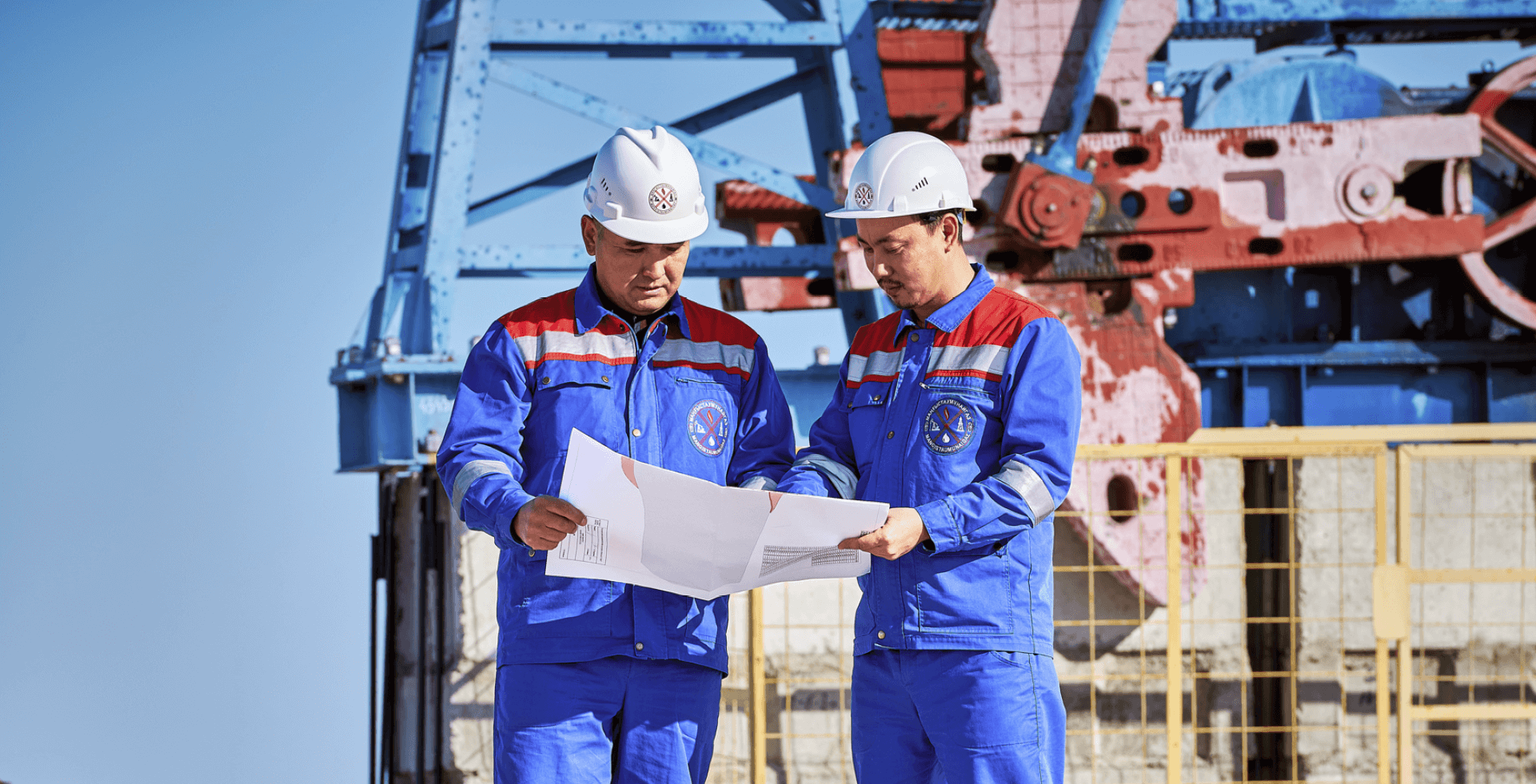 Два работника на фоне буровой установки